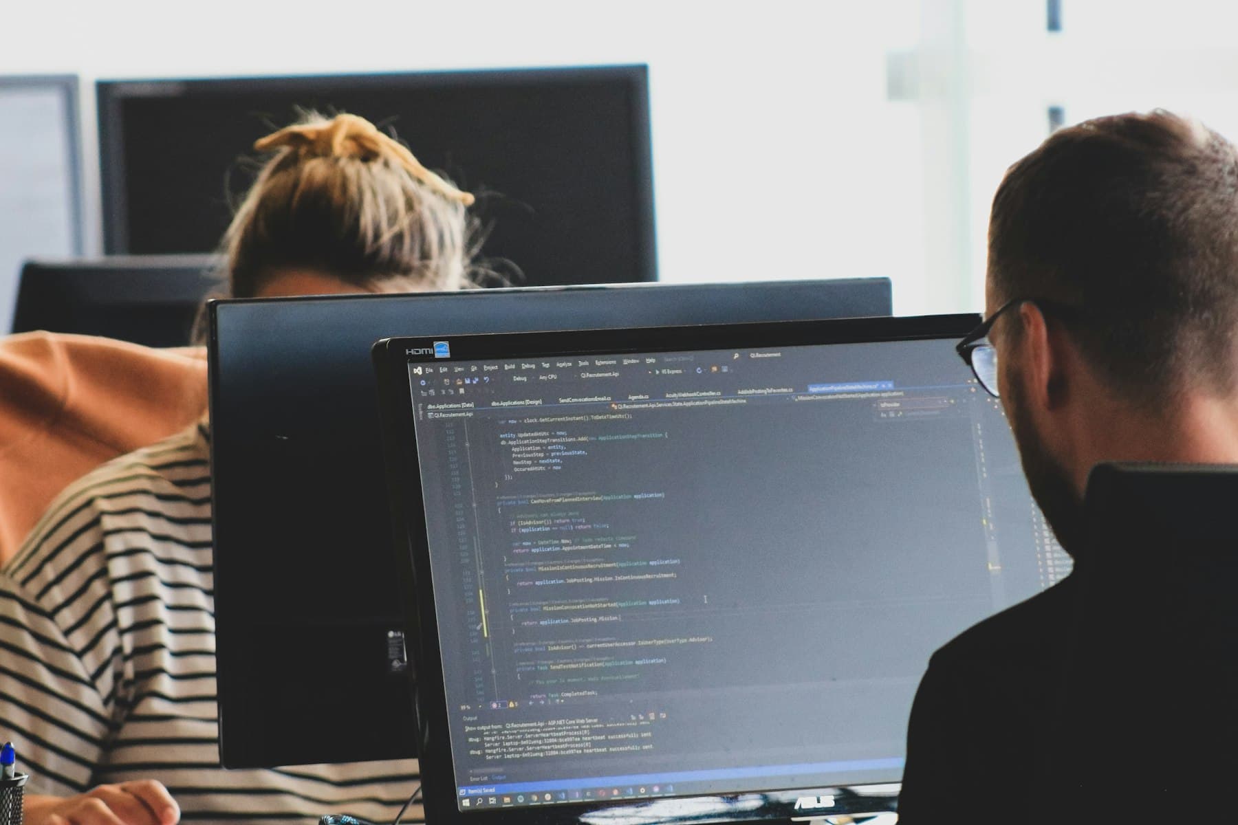 Two people working on code at monitors in a bright office