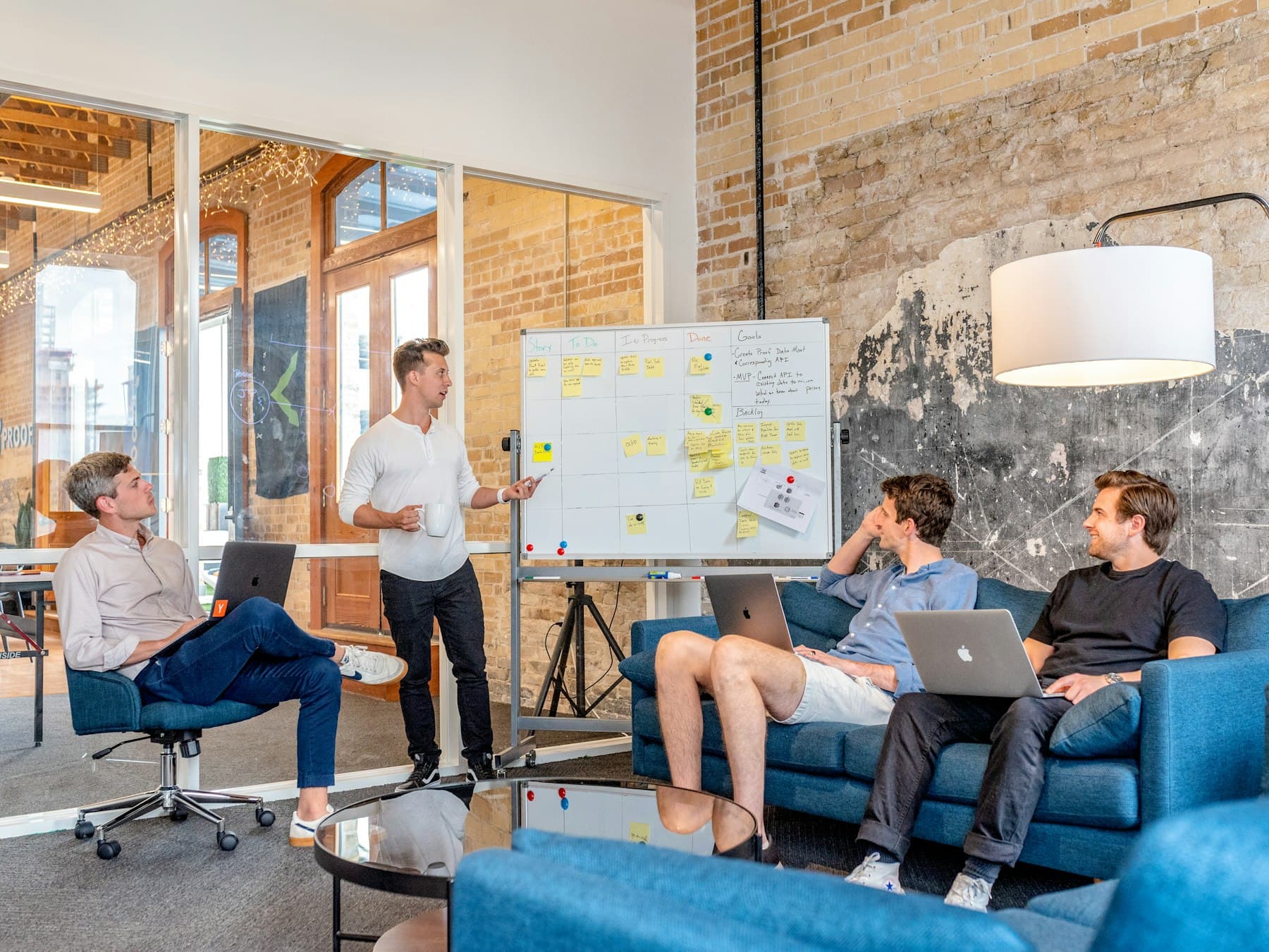 A small team with laptops listening to a colleague at a whiteboard