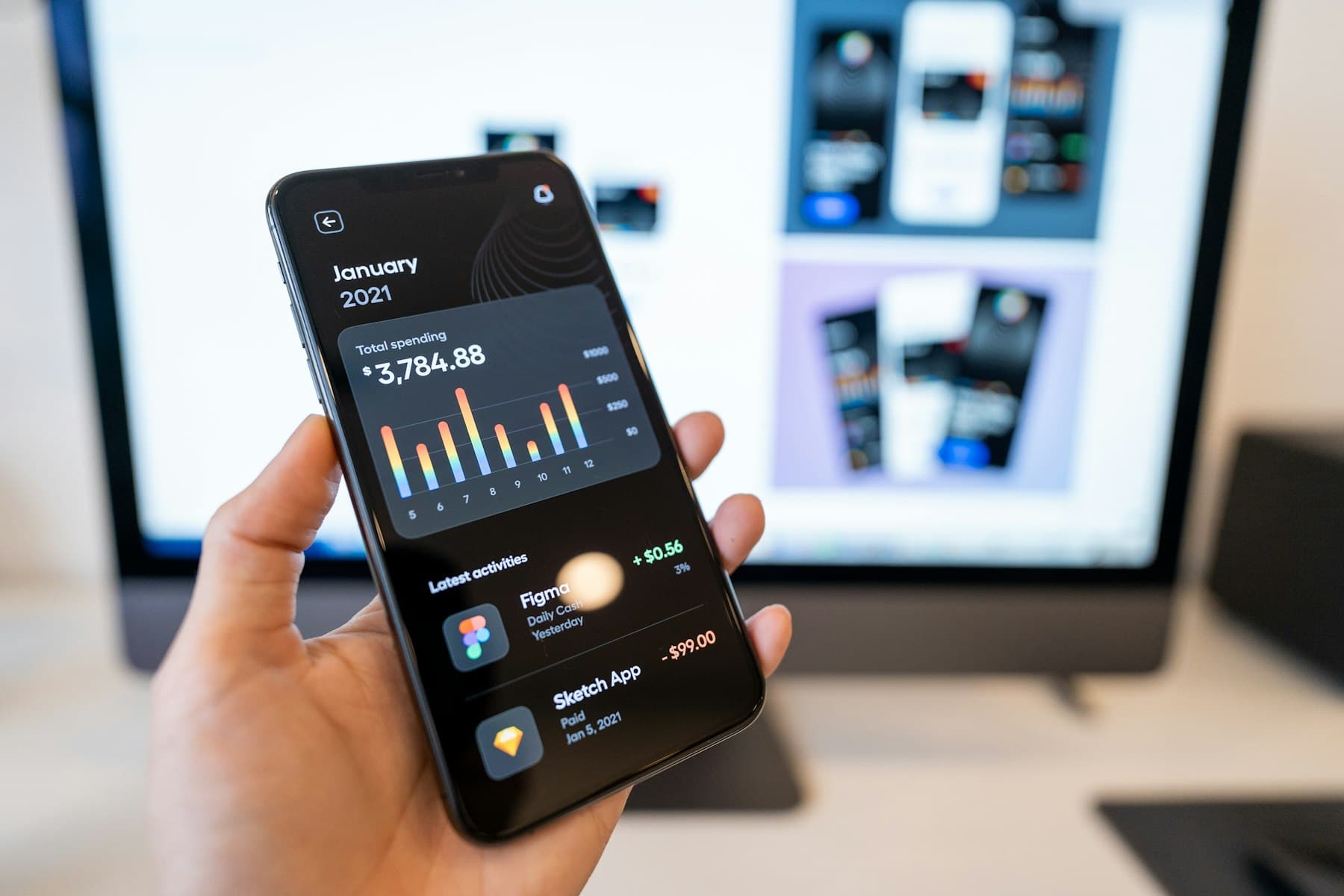 A hand holding a phone showing a spending dashboard